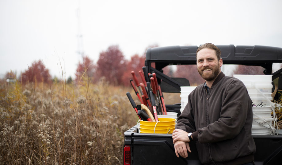 Remis Ensweiller stands in the prairie next to his golf cart filled with gardening supplies