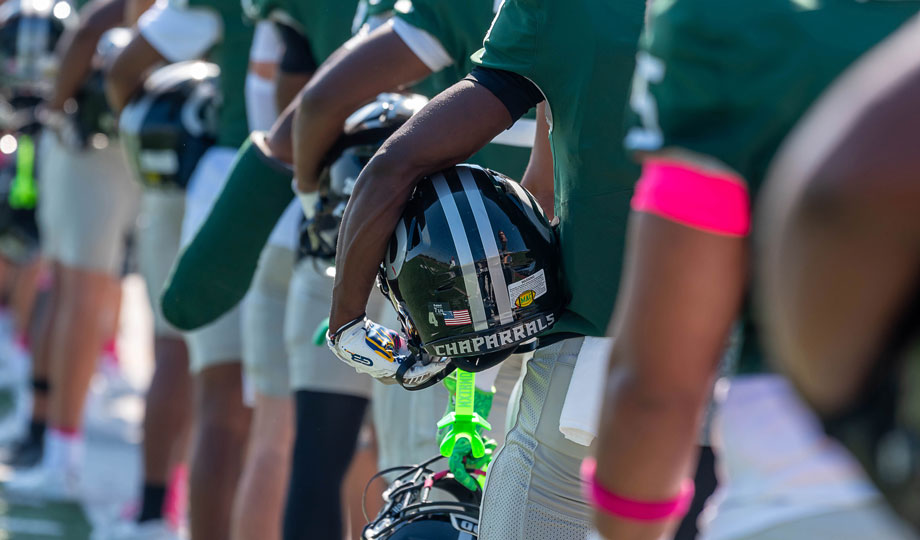 Football player holding helmet under arm on sideline.